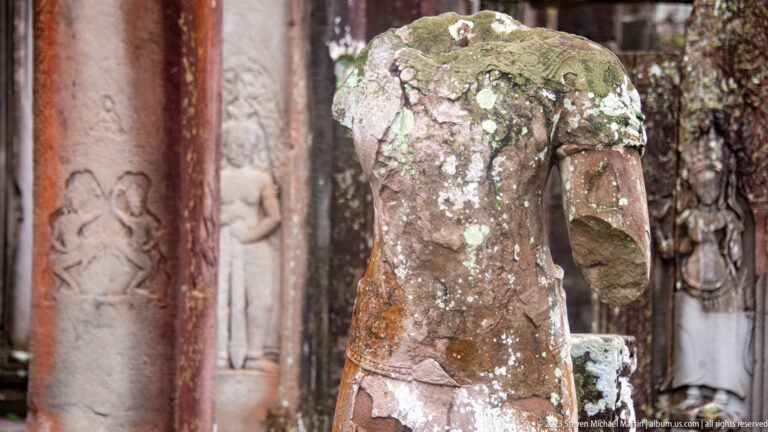Close view of a lichen-covered headless sandstone torso with one surviving arm at Bayon.