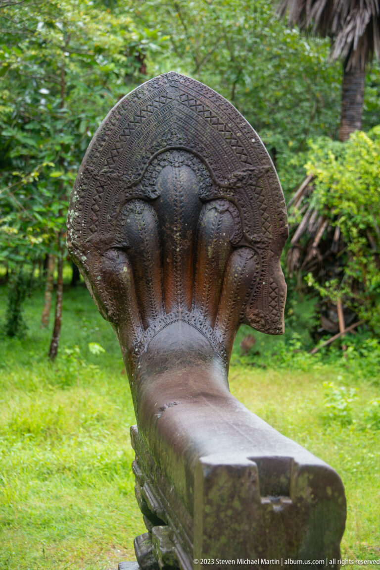 Weathered stone naga with a fan of multiple cobra heads at the end of a balustrade.