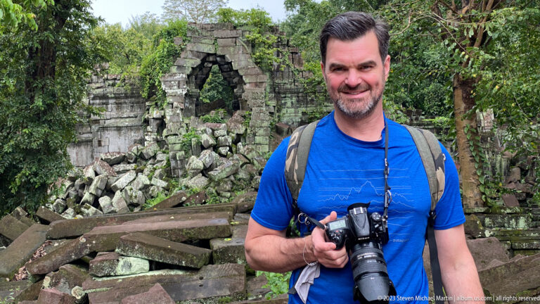 Male traveler with a camera stands before a collapsed stone opening at Beng Mealea.