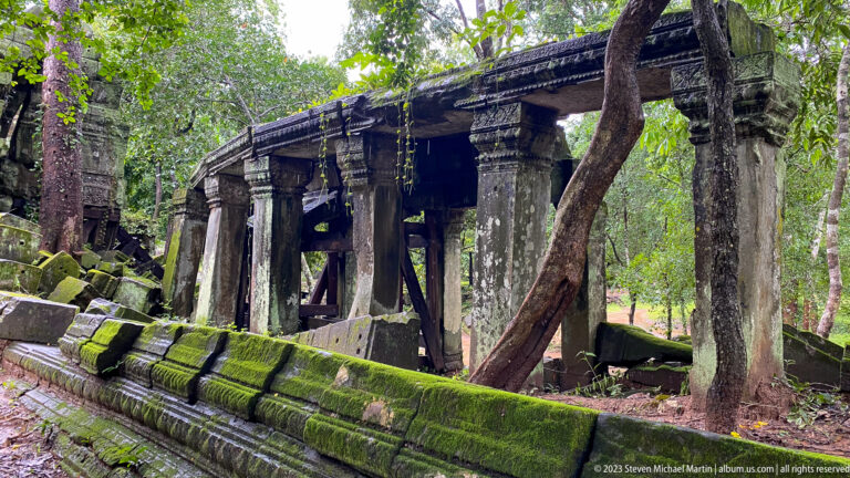 Long moss-covered sandstone gallery reinforced by heavy timber braces beneath forest trees.