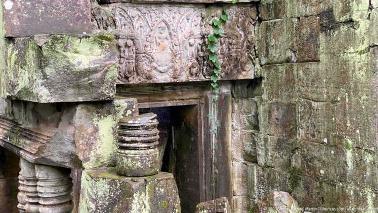 Carved sandstone doorway with relief panels and a displaced turned stone fragment at Beng Mealea.