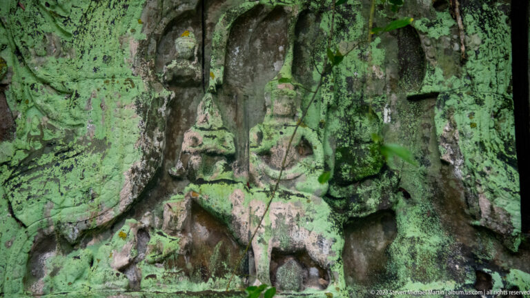 Close detail of an eroded female temple figure partly hidden beneath green lichen and staining.