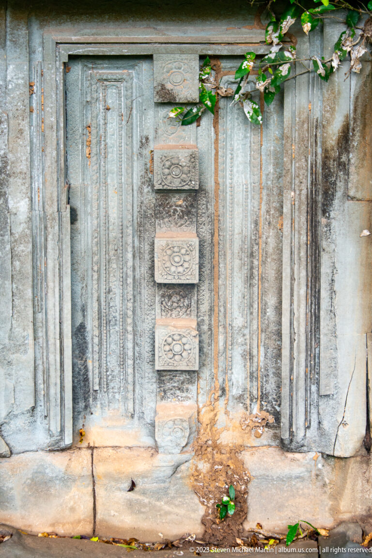Close view of a sandstone wall base with colonnettes, recessed panels, and small floral motifs.