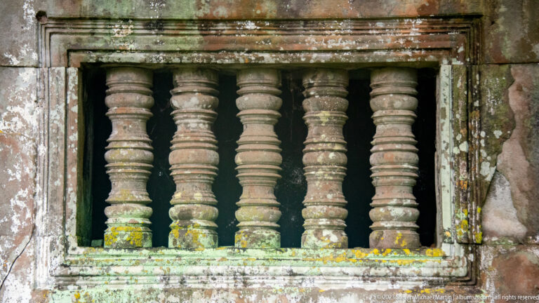 Rectangular temple window containing five turned sandstone balusters with lichen and weather staining.