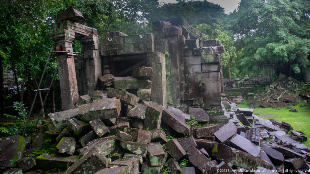 Collapsed stone entrance filled with fallen blocks and braced by a modern metal support frame.
