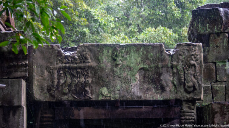 Weathered carved lintel above a dark opening with a central figure and scrolling ornament.