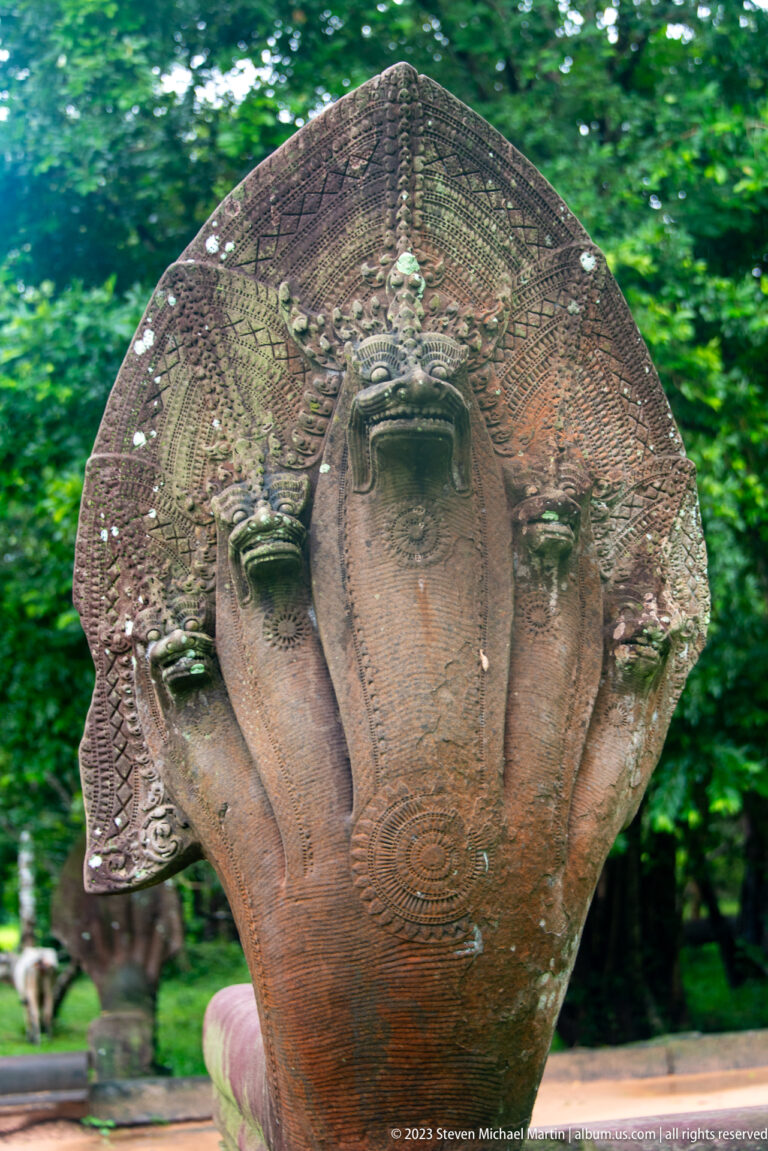 Close view of a weathered seven-headed sandstone naga with fanned cobra hoods and carved scales.