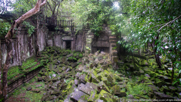 Enclosed temple area densely filled with mossy fallen sandstone blocks and surviving doorways.
