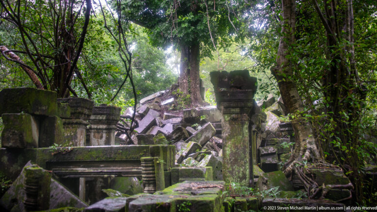 Standing sandstone posts framing a forested passage filled with a deep pile of fallen blocks.