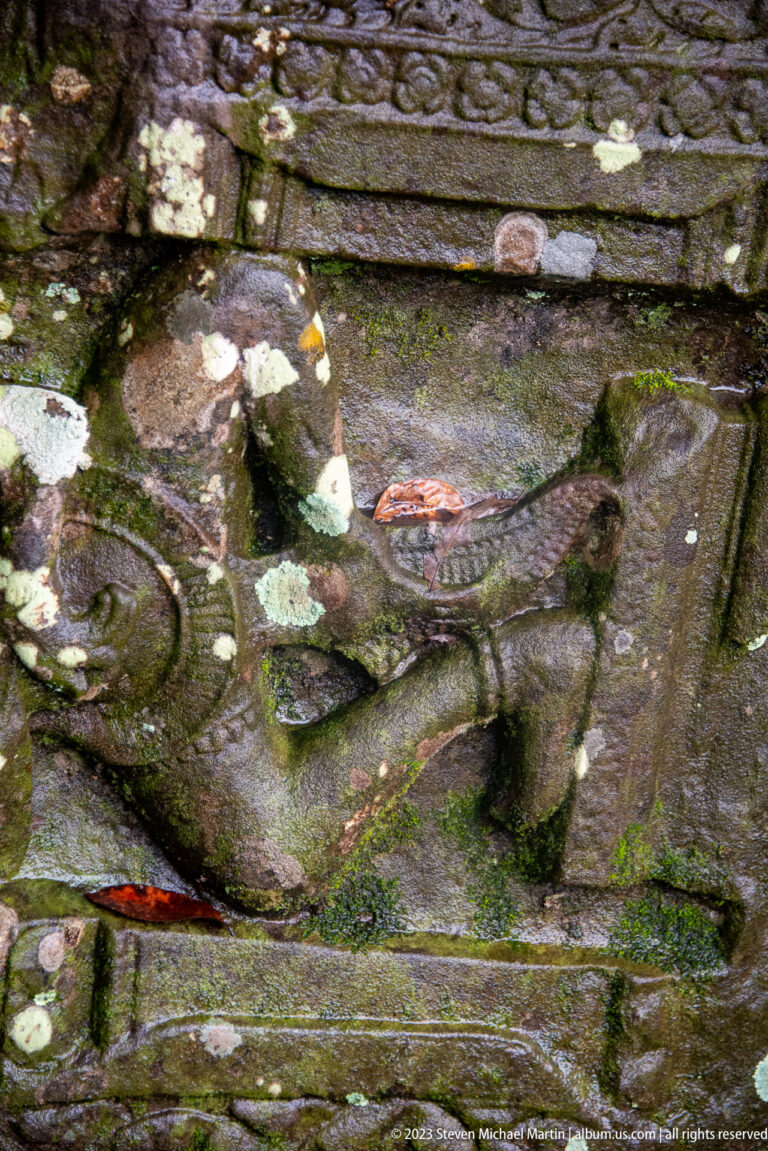 Close weathered sandstone relief of a human figure partly obscured by lichen and staining.