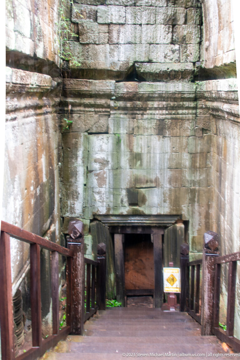 Wooden platform leading to a low rectangular doorway in a stained sandstone temple wall.