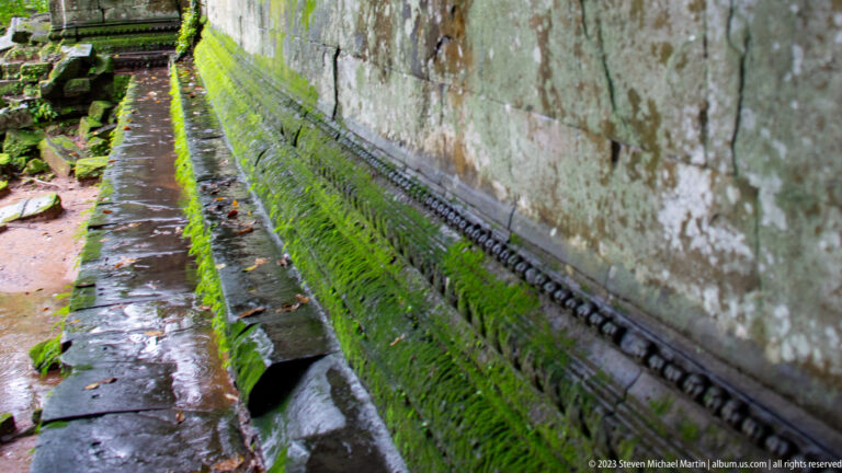 Moss-covered sandstone wall base with bead molding and a narrow water channel.