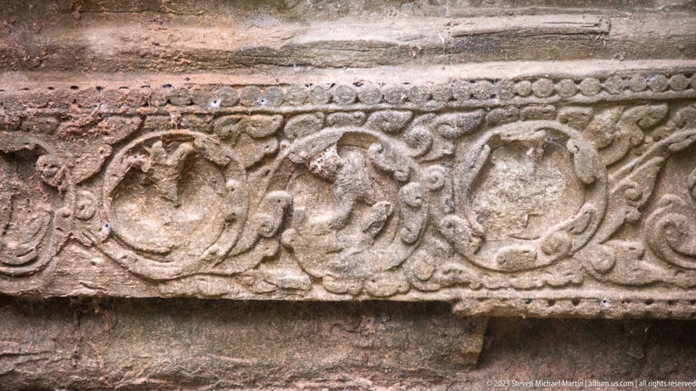 Sandstone frieze with repeated circular medallions, curling foliage, and a beaded upper border.