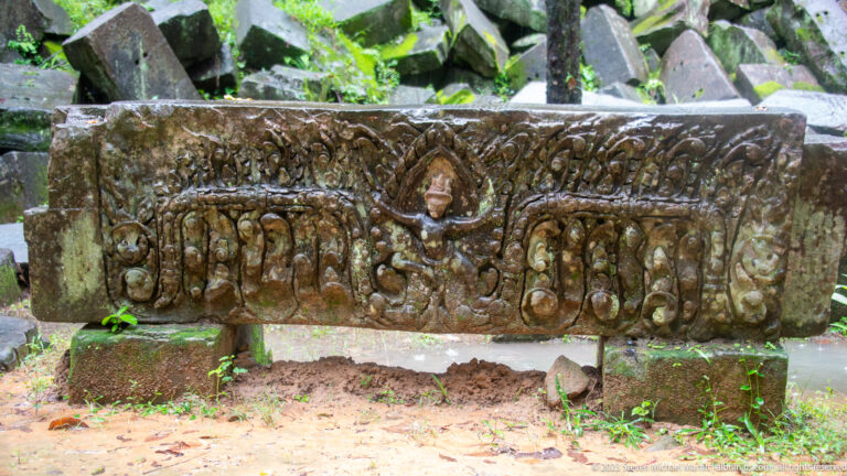 Upright carved sandstone lintel with a central figure and dense symmetrical scrollwork.