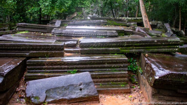 Large pile of displaced sandstone cornices, bases, and long architectural moldings within the ruins.