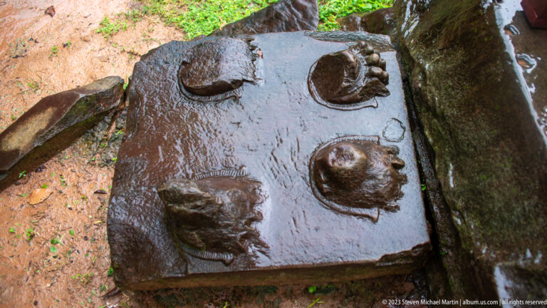 Wet rectangular sandstone slab with four raised circular carved bosses arranged in a grid.