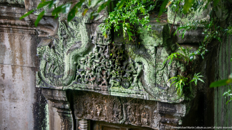 Ornate sandstone lintel with foliate and figurative carving above a dark doorway at Beng Mealea.