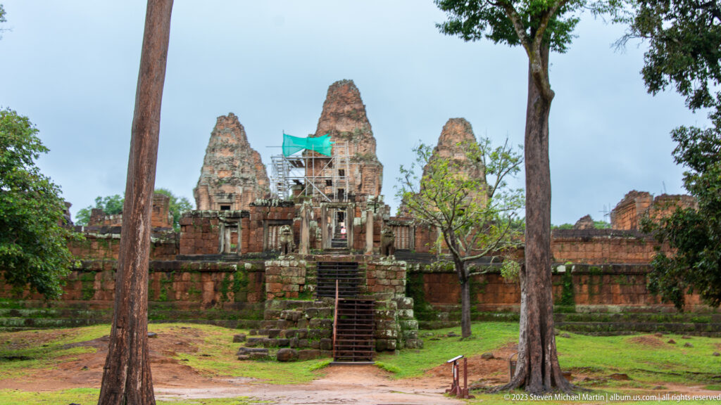 Frontal view of East Mebon’s brick sanctuary towers above a raised stair, framed by trees and laterite walls.