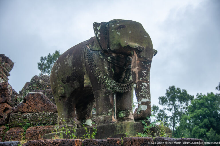 Low-angle three-quarter view of stone elephant on temple terrace.