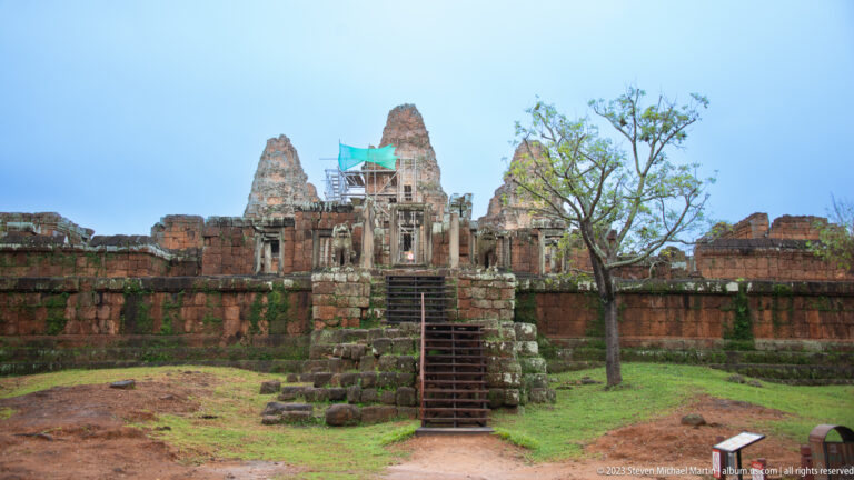 Axial view of East Mebon’s entrance stair, laterite platform, and brick sanctuary towers with scaffolding at center.