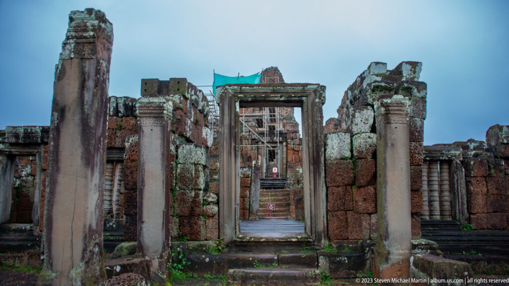 Aligned stone doorways and columns create an axial passage toward a scaffolded sanctuary tower at East Mebon.