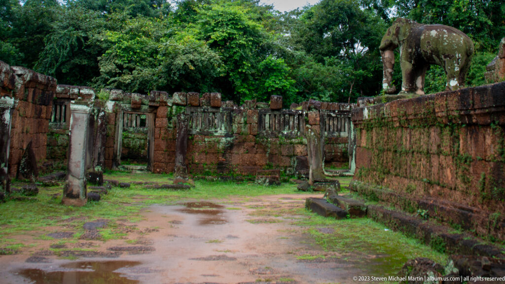 Temple courtyard with laterite walls and stone elephant statue above the enclosure.