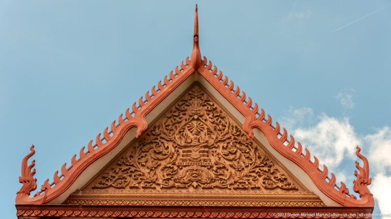Triangular museum pediment filled with Khmer-style relief carving, red trim, and curling roof finials.