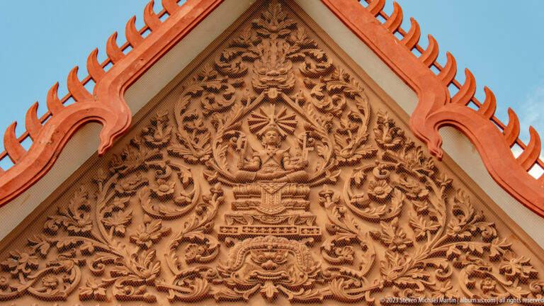 Close view of ornate gable relief with a seated deity, scrolling foliage, and an open-mouthed creature below.