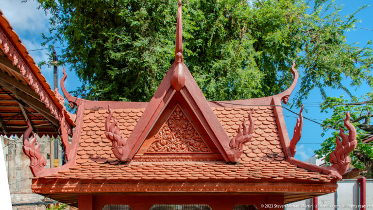 Close view of a red tiled roof with an ornate triangular gable, carved ornament, and tall curling finials.
