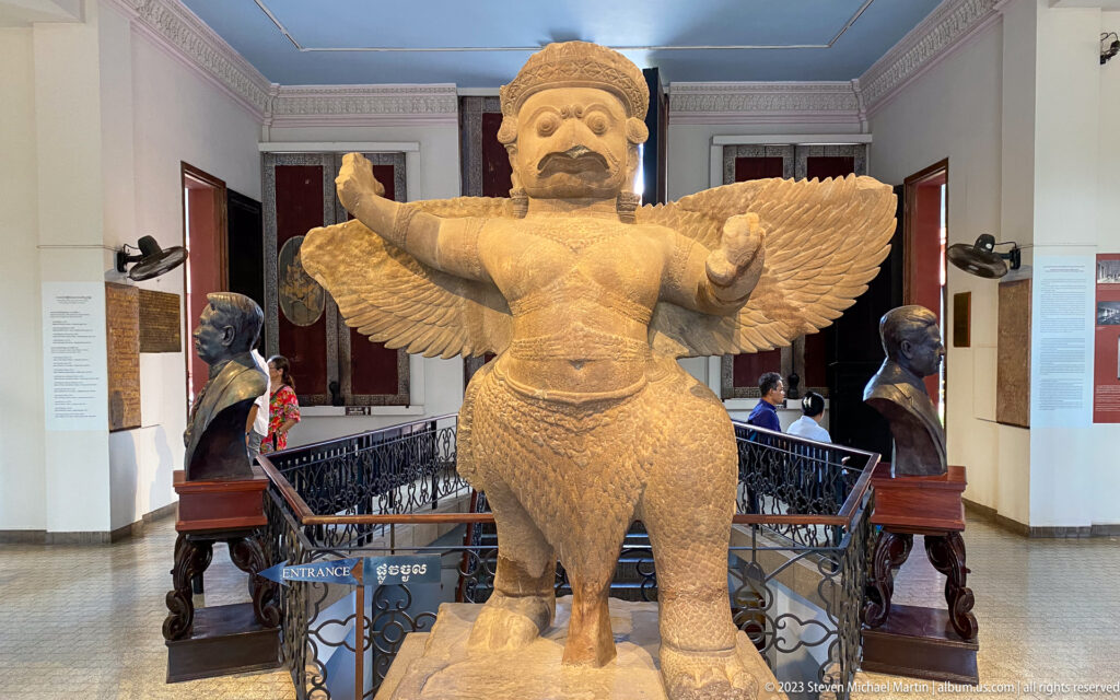 Monumental pale stone Garuda with outstretched arms and broad wings standing at the museum stair.