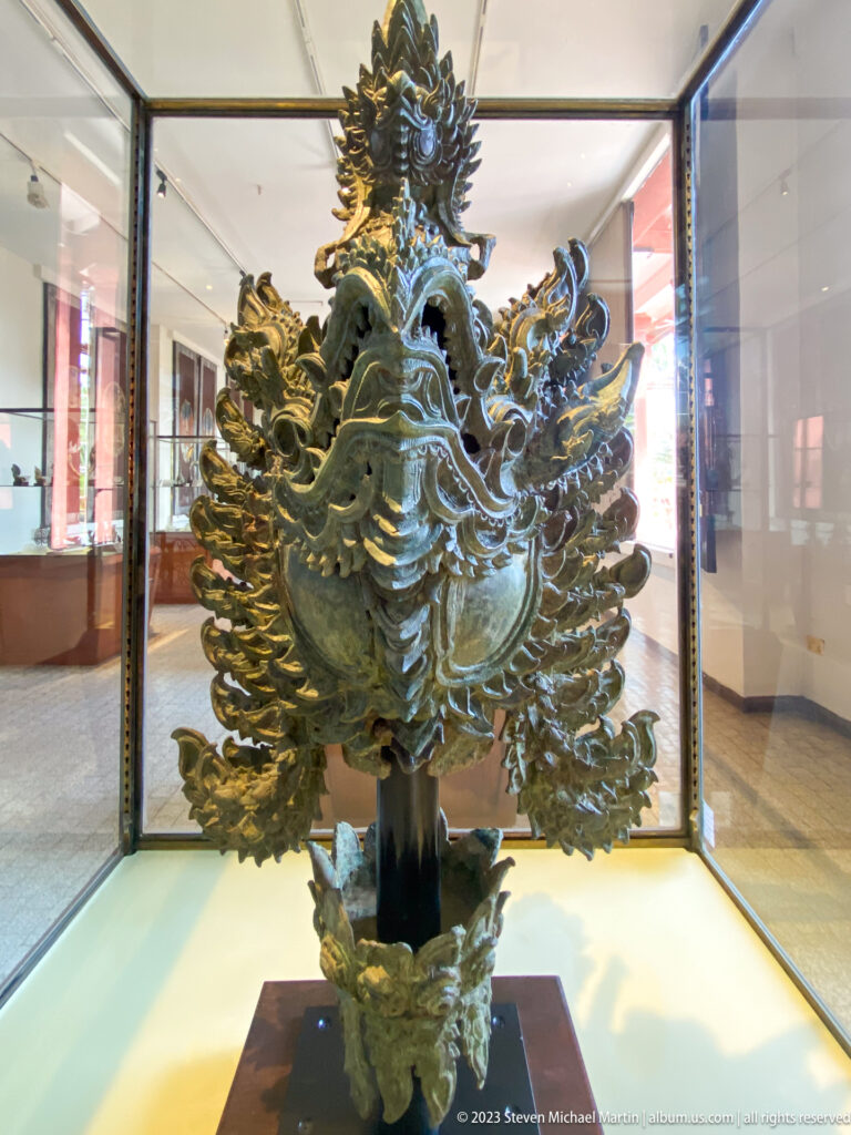 Large bronze openwork crest with a central bird-like form, flame motifs, and a narrow supporting stem.