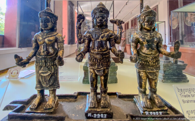Three standing bronze deities with tall headdresses, jewelry, patterned garments, and varied hand gestures.