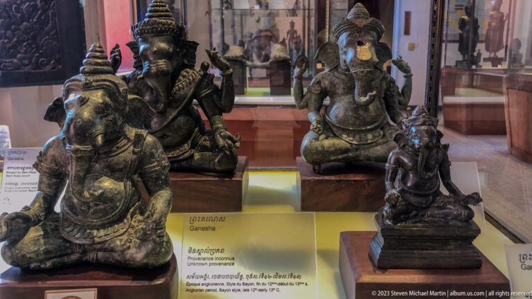 Several seated bronze Ganesha figures of different sizes displayed together behind glass.