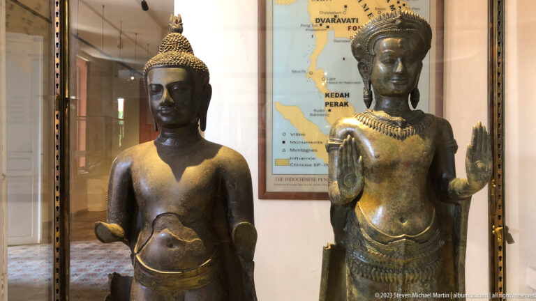 Two standing bronze Buddhist figures with crowns and jewelry displayed together inside a museum case.