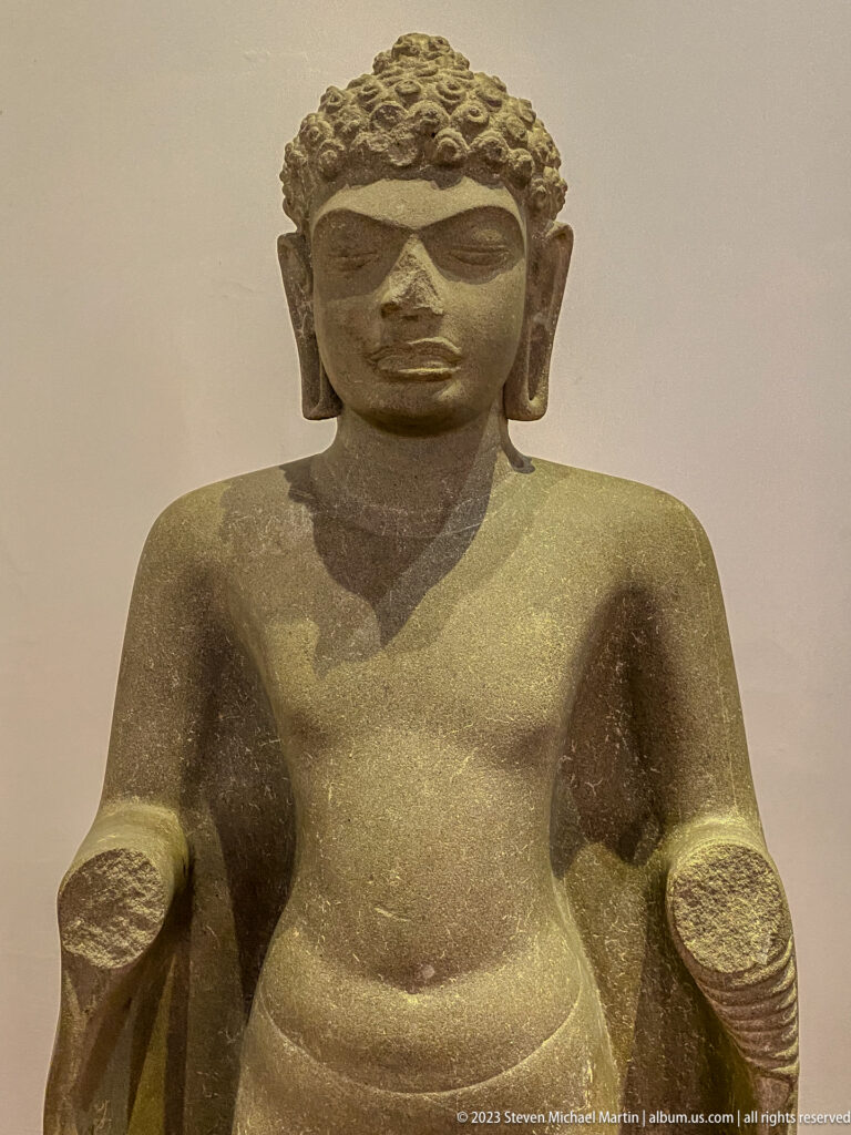 Large frontal stone Buddha with curled hair, elongated earlobes, and weathered surface.