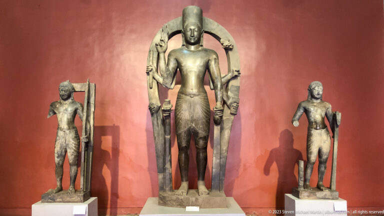 Central standing figure with attendants displayed in the National Museum of Cambodia gallery.