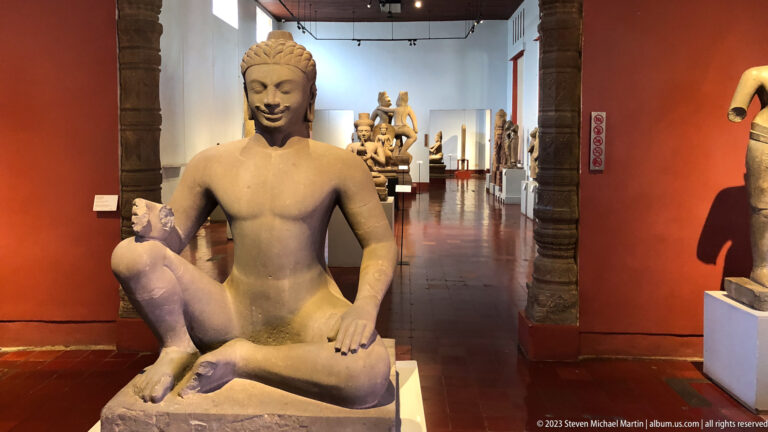 Seated Khmer stone figure displayed in the National Museum of Cambodia gallery.