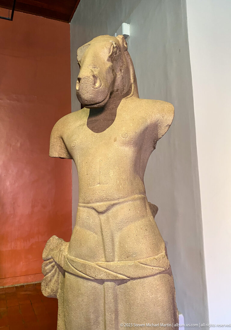 Horse-headed anthropomorphic sandstone torso displayed in the National Museum of Cambodia gallery.