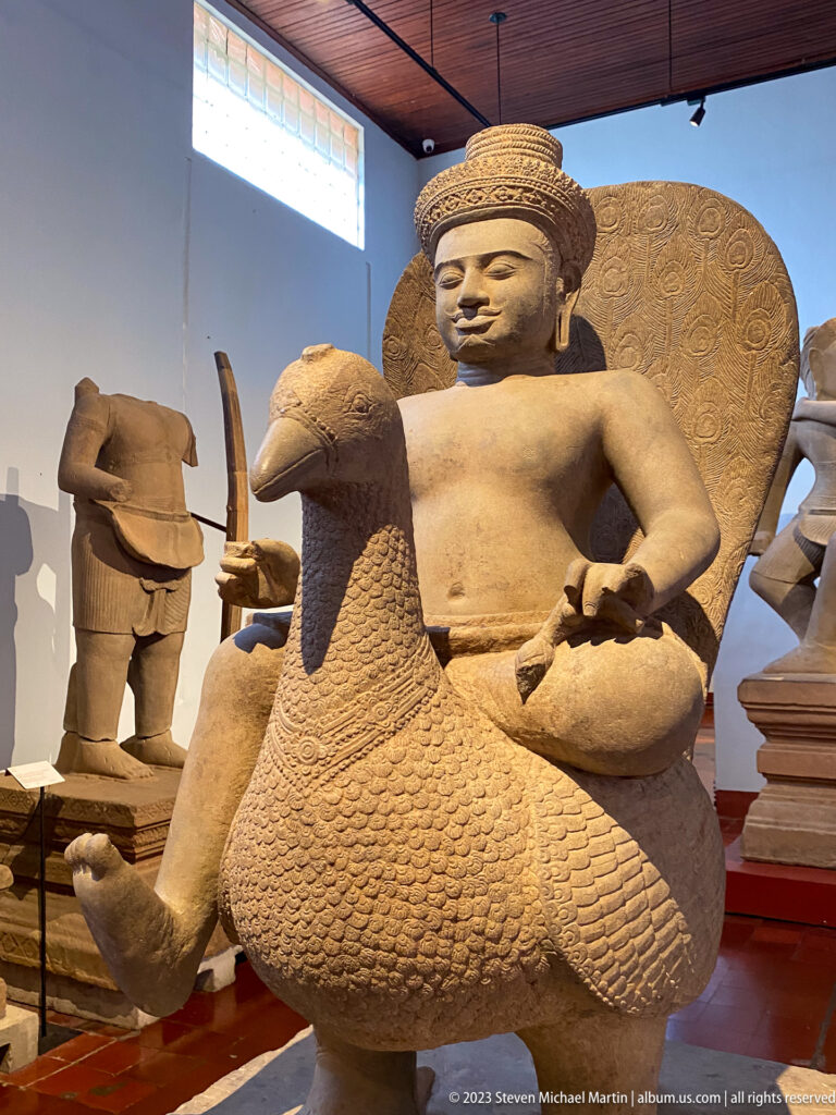 Close view of seated deity on bird mount displayed in the National Museum of Cambodia gallery.