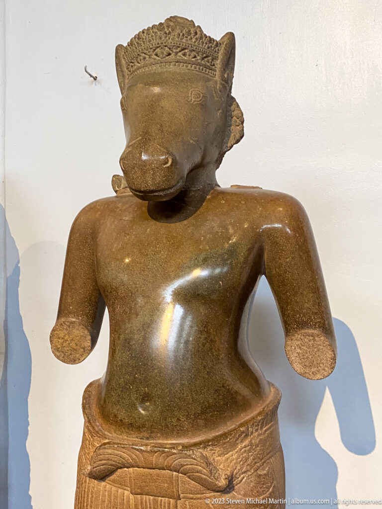 Boar-headed anthropomorphic sandstone figure displayed in the National Museum of Cambodia gallery.