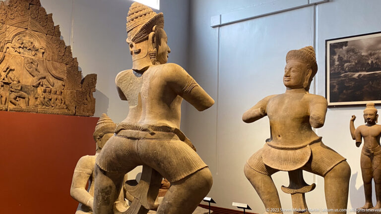 Rear view of monumental standing Khmer sculptures displayed in the National Museum of Cambodia gallery.