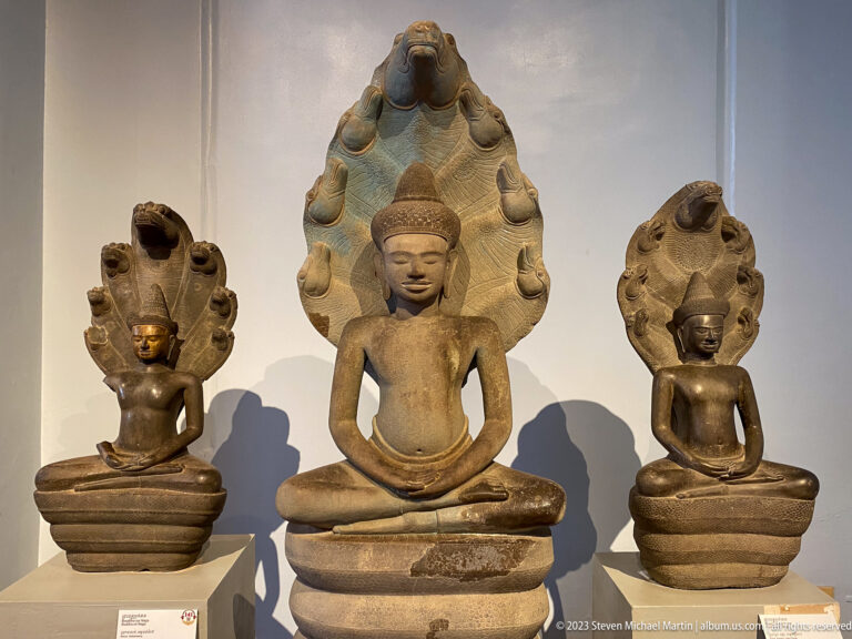 Three seated Buddhas sheltered by naga hoods displayed in the National Museum of Cambodia gallery.