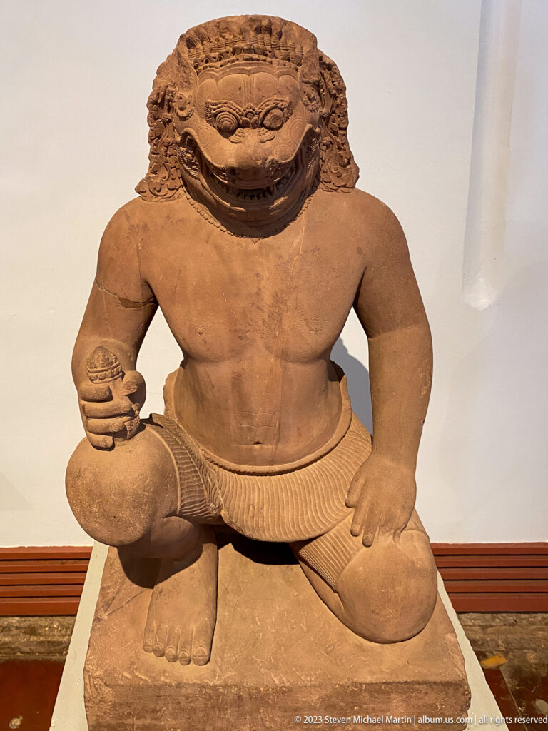 Kneeling lion-headed guardian sculpture displayed in the National Museum of Cambodia gallery.