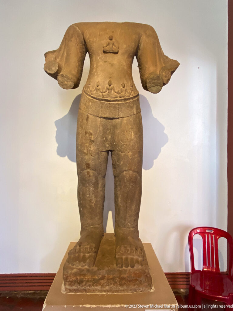 Headless sandstone torso preserving carved garment, belt, feet, and portions of both arms.