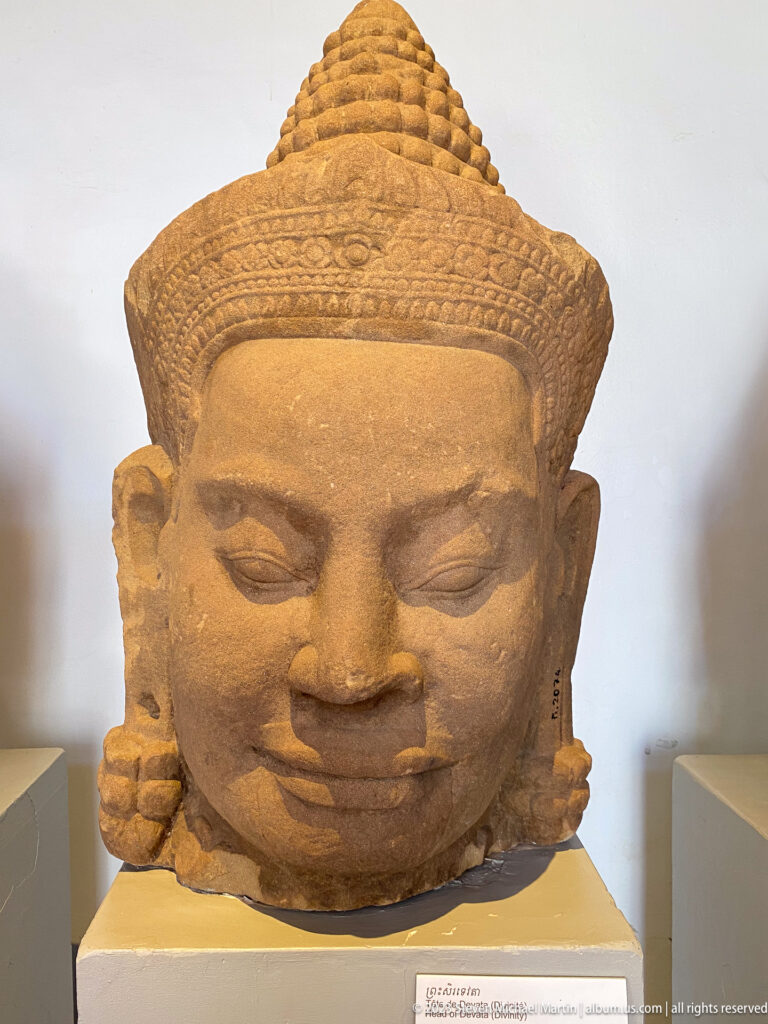 Monumental sandstone Buddha head with curled hair, elongated earlobes, and serene expression.
