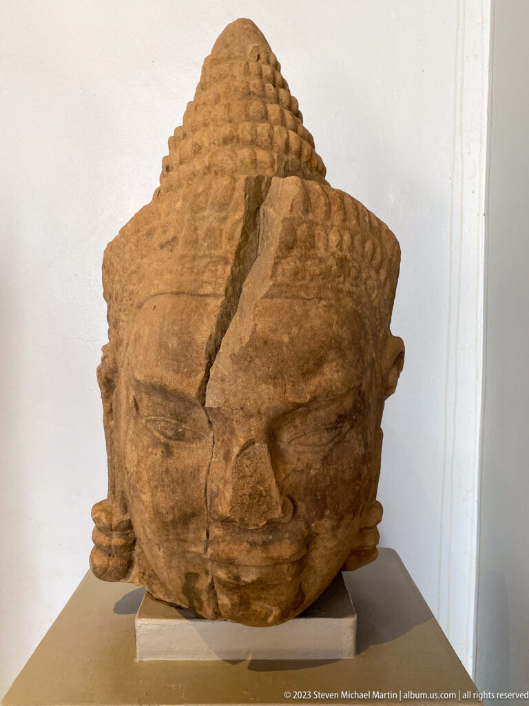 Fractured sandstone Buddha head with curled hair, elongated earlobes, and a calm face.