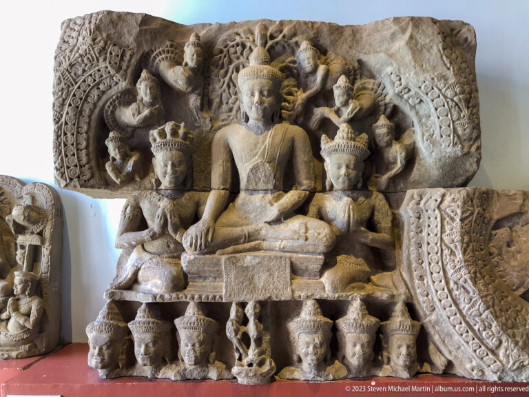 Large seated Buddha flanked by crowned attendants beneath an ornate carved architectural canopy.