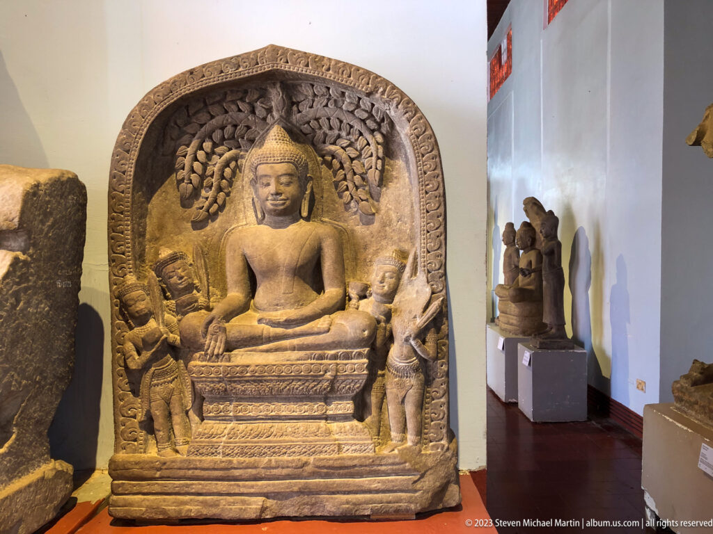 Seated Buddha inside a carved niche framed by attendants, foliage, and decorative borders.