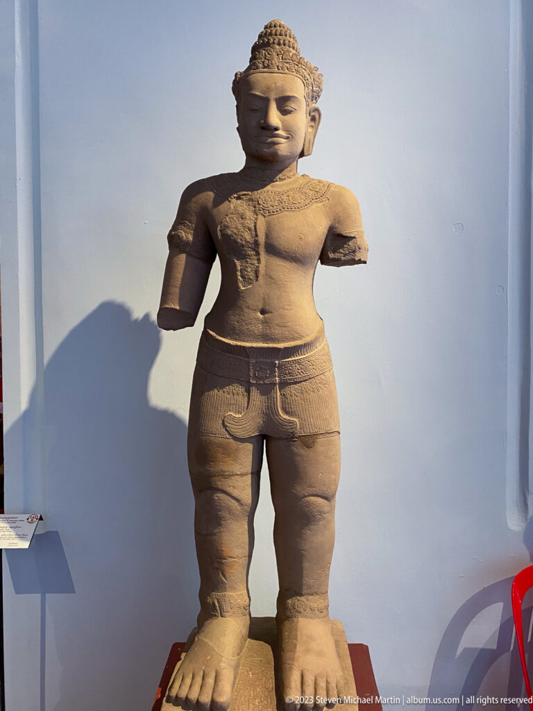 Fragmentary standing Buddha with curled hair, elongated earlobes, and both forearms missing.