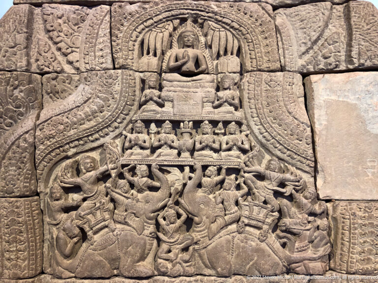 Seated Buddha above a crowded narrative register of warriors, attendants, and intertwined figures.